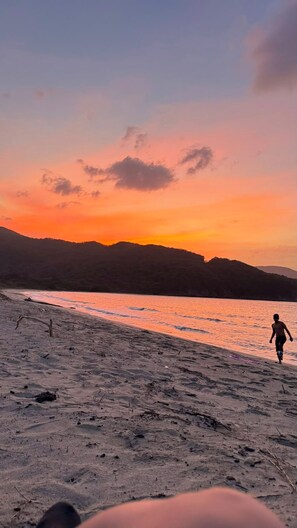 Een strand met een persoon die langs de kust loopt tijdens de zonsondergang.