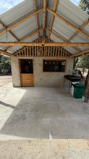 A covered outdoor area with a concrete floor, a wooden door, and a window.