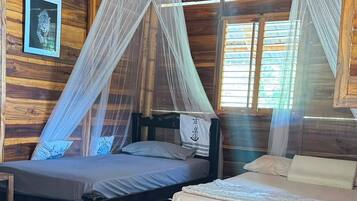Habitación con dos camas, piso de madera, mosquitero y un cuadro en la pared.