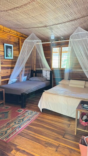A room with two beds, each with a canopy, wooden walls, and a patterned rug.