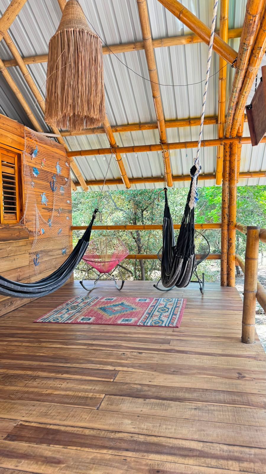 A hammock suspended from a bamboo structure, a woven basket, and a patterned rug on a wooden deck.