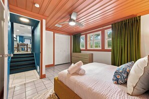 Ein Schlafzimmer mit einem Bett, einem Deckenventilator, einem Fenster mit Vorhängen und einer Treppe, die zu einem Badezimmer führt.
