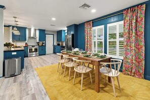 Eine moderne Küche mit blauen Schränken, ein Essbereich mit einem Holztisch und -stühlen sowie ein gelber Teppich.