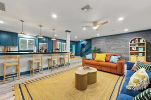 A modern living room with a sofa, coffee table, and a kitchen area with bar stools. - Sauna • Cold Plunge • Sports Court • Pool • Hottub (Bradenton)