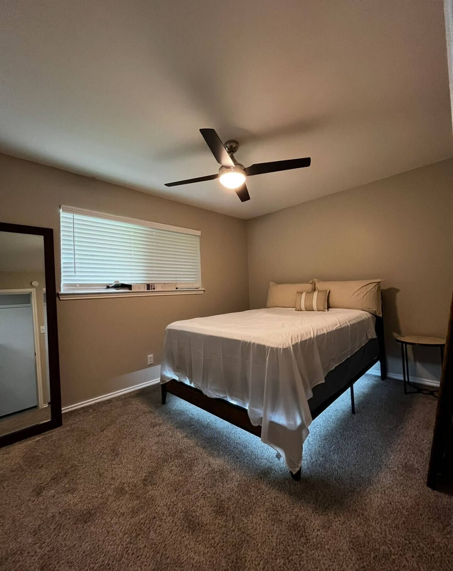 A bedroom with a bed, a ceiling fan, a window with blinds, and a carpeted floor.