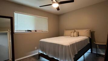 A bedroom with a bed, a ceiling fan, a window with blinds, and a carpeted floor.