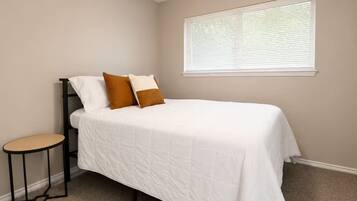 A bedroom with a bed, a ceiling fan, a window with blinds, and a small table.