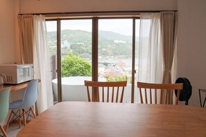 A room with a dining table, two chairs, a microwave, and a view of a hilly landscape through large windows. - A private villa with an open-air hot spring bath offering panoramic views of the ocean and the port town! Complete with a slide and a movie projector—enjoy a special getaway for up to 8 guests (Inatori, Higashiizu, Kamo District)