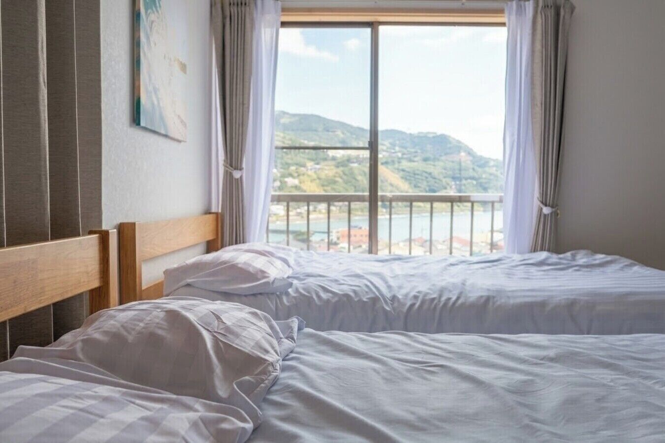 A bedroom with two beds, a view of a body of water and hills, and a balcony with curtains.