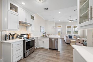 A modern kitchen with white cabinetry, stainless steel appliances, and a wooden floor. - Casa de Miramar 4BR/3BA with 3 King Beds and Beach, Pool & Fishing Pier Access (Galveston)