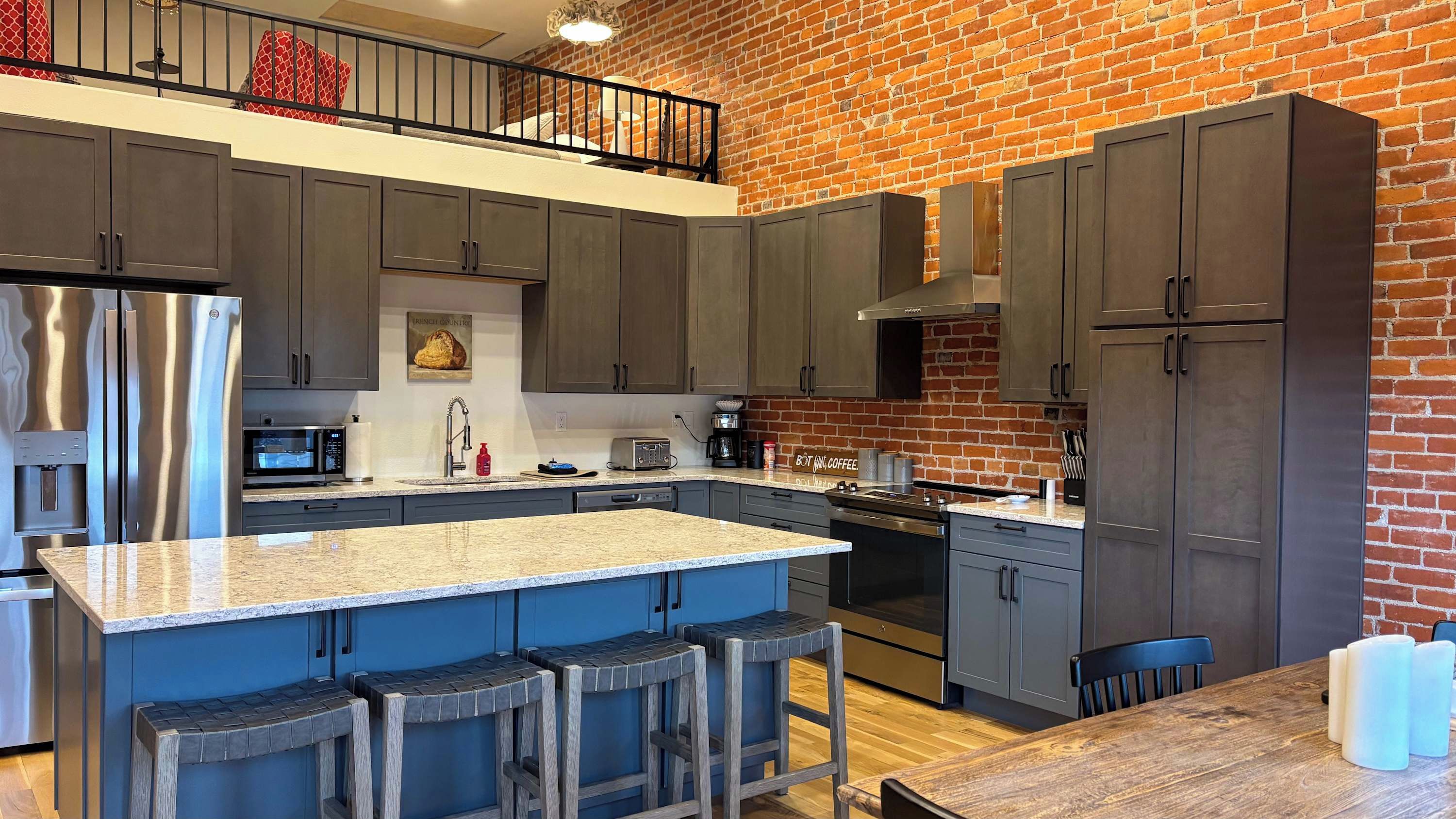 Et moderne køkken med en central ø, mørke skabe og en murstensvæg.