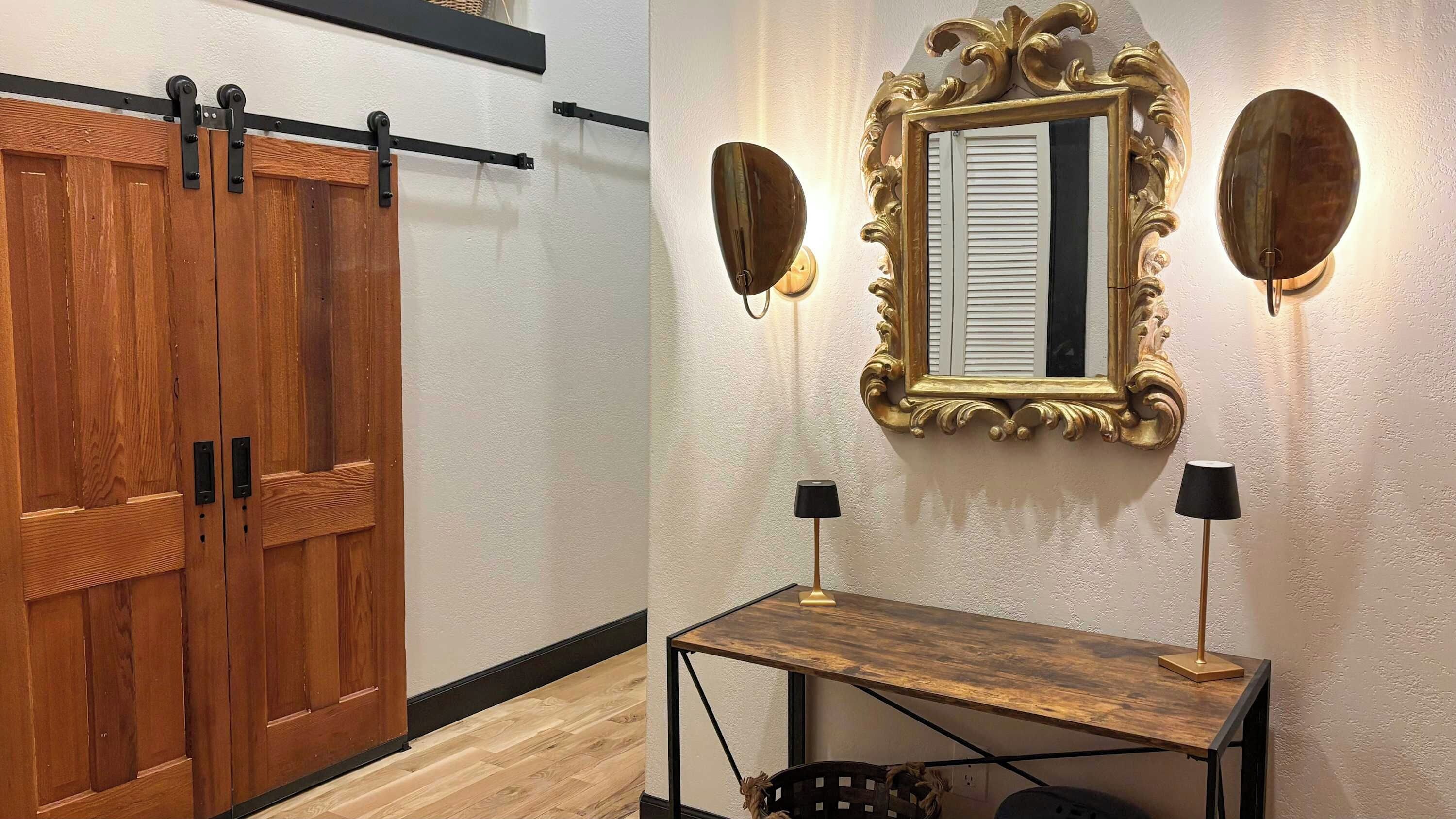 A room with a wooden sliding door, a mirror with an ornate frame, and a small table with two lamps.
