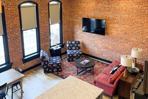 Ein Zimmer mit Backsteinwand, einem flachbildfernseher über einer Couch, einem Esstisch mit Stühlen und einem gemusterten Teppich.