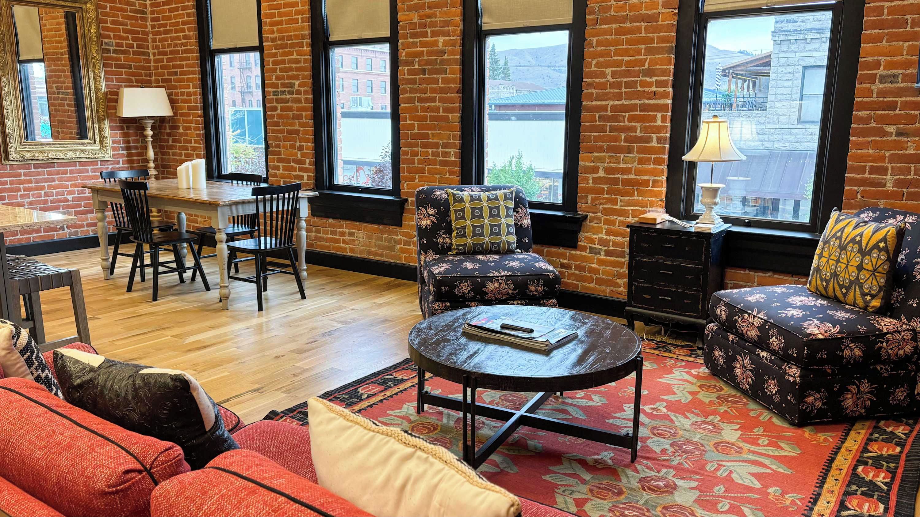 A room with a brick wall, a dining table with chairs, a sofa, a round coffee table, and a patterned rug.