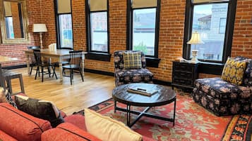 A room with a brick wall, a dining table with chairs, a sofa, a round coffee table, and a patterned rug.