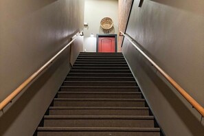 A carpeted staircase with handrails, leading to a door with a basket on the wall above it. - Fishers Loft A , Luxury Downtown Loft w/ Panoramic Views (Baker City)