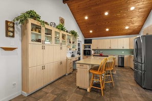 A modern kitchen with wooden cabinets, a stainless steel refrigerator, and a wooden dining area. - Rogue Beach House Uppper Level (Gold Beach)