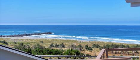 A coastal view with a beach, ocean, and a road leading to a house with a balcony.
