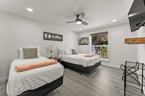 Un dormitorio con dos camas, un ventilador de techo, una ventana con vistas y un televisor montado en la pared.