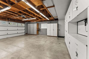 Ein geräumiges Zimmer mit hohen Decken, freiliegenden Holzbalken und einem Betonboden. Es beinhaltet mehrere weiße Schließfächer und ein großes Fenster mit Jalousien.