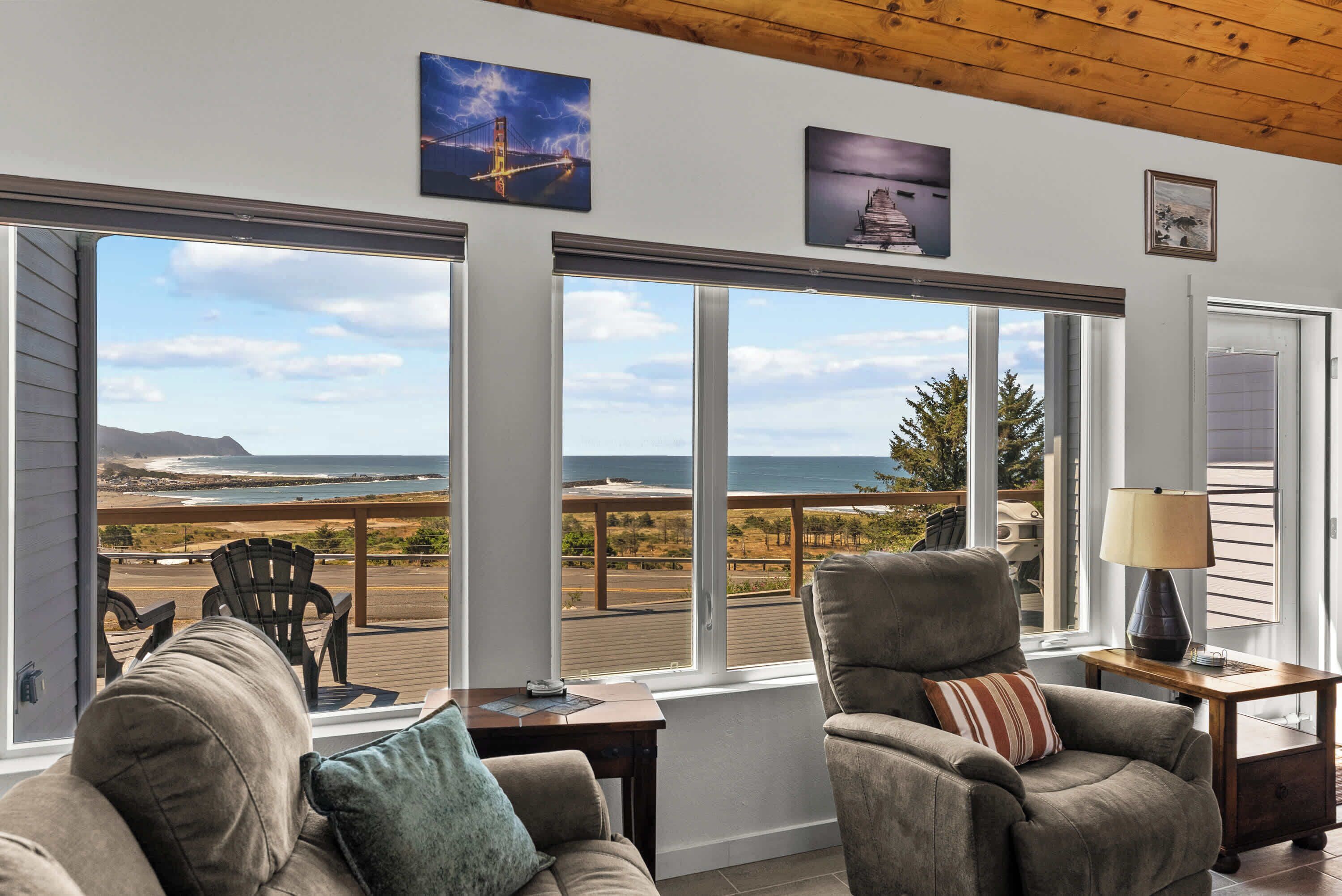 A room with large windows overlooking a beach and ocean, furnished with two armchairs and a small table.