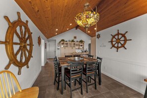 A dining area with a wooden ceiling, a chandelier, and two ship wheels on the walls. - Rogue Beach House Uppper Level (Gold Beach)
