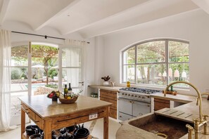 A kitchen with a gas stove, sink, and a view of a pool and garden through large windows. - Ca´n Lull – Unique finca within olive grove, bespoke amenities (max. 10 guests) (Marratxi)