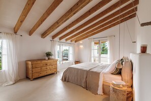 Ett sovrum med ett träpanelat tak, en säng med ett beige överkast, en byrå och ett sängbord med en lampa.