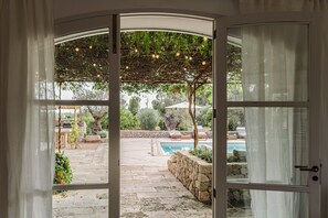 Ein offener Durchgang zu einer Terrasse mit Pool, Steinböden, Gartenmöbeln und einer Pergola mit Lichterketten.