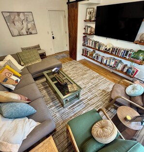 Een woonkamer met een bank, fauteuil, salontafel, boekenkast en een flatscreen televisie.