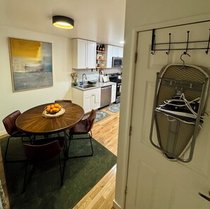 A dining area with a table set for four, a kitchen in the background, and a door with a coat rack. - 2BR/2BA in Andersonville · pet-friendly · workspace · garage parking · king beds (Chicago)