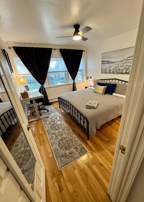 A bedroom with a bed, a desk, a chair, a window with curtains, a ceiling fan, and a painting on the wall. - 2BR/2BA in Andersonville · pet-friendly · workspace · garage parking · king beds (Chicago)