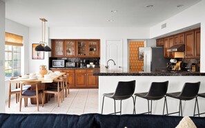 A modern kitchen with wooden cabinets, a dining area with a table and chairs, and a bar area with stools. - Designer Home • Free Heated Pool • BBQ • Game Room • Garage • Sleeps 16 (Gilbert)