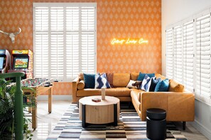 A living room with a sectional sofa, a foosball table, and a neon sign. - Designer Home • Free Heated Pool • BBQ • Game Room • Garage • Sleeps 16 (Gilbert)