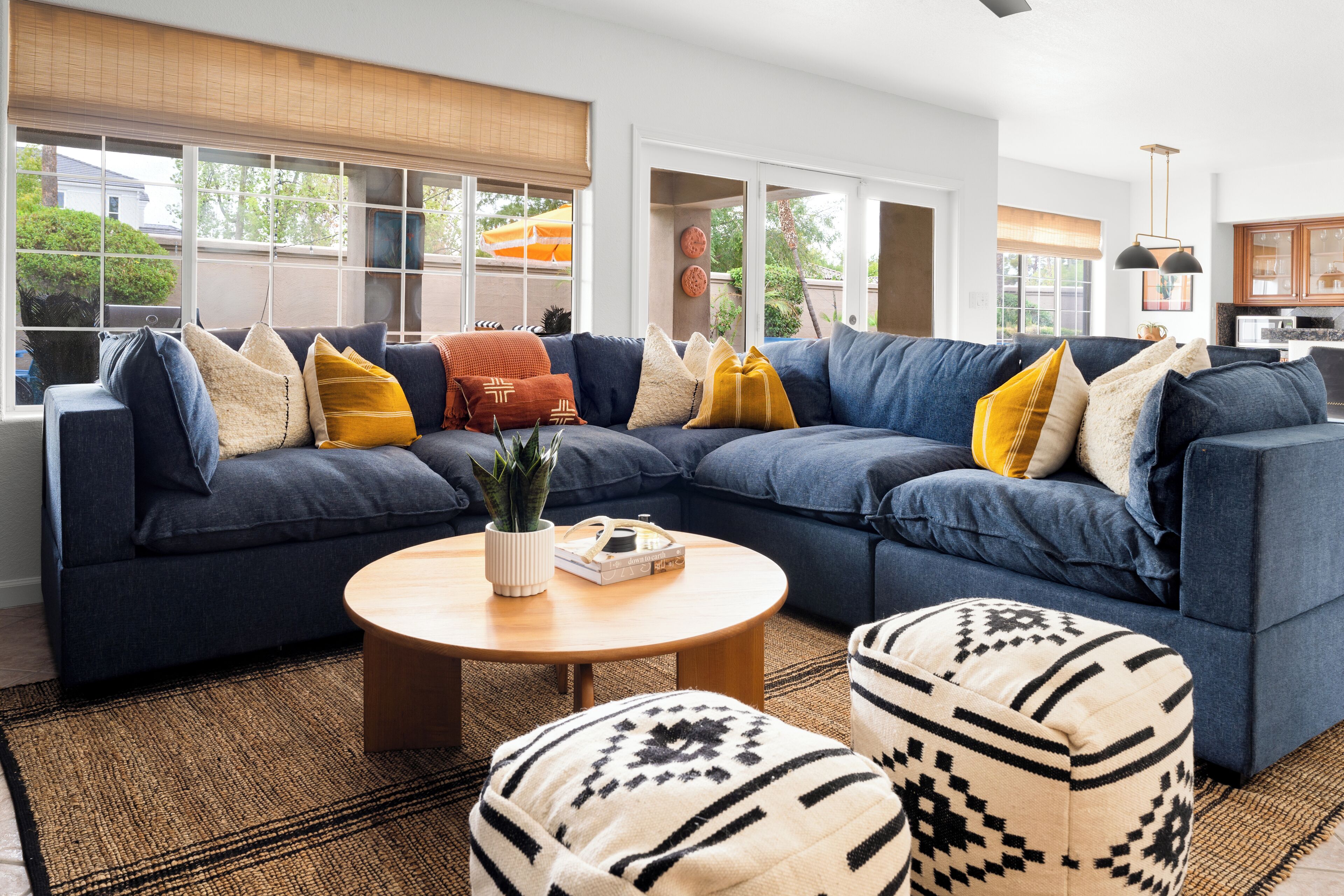 Un salon moderne avec un canapé d’angle, une table basse ronde et des poufs à motifs.