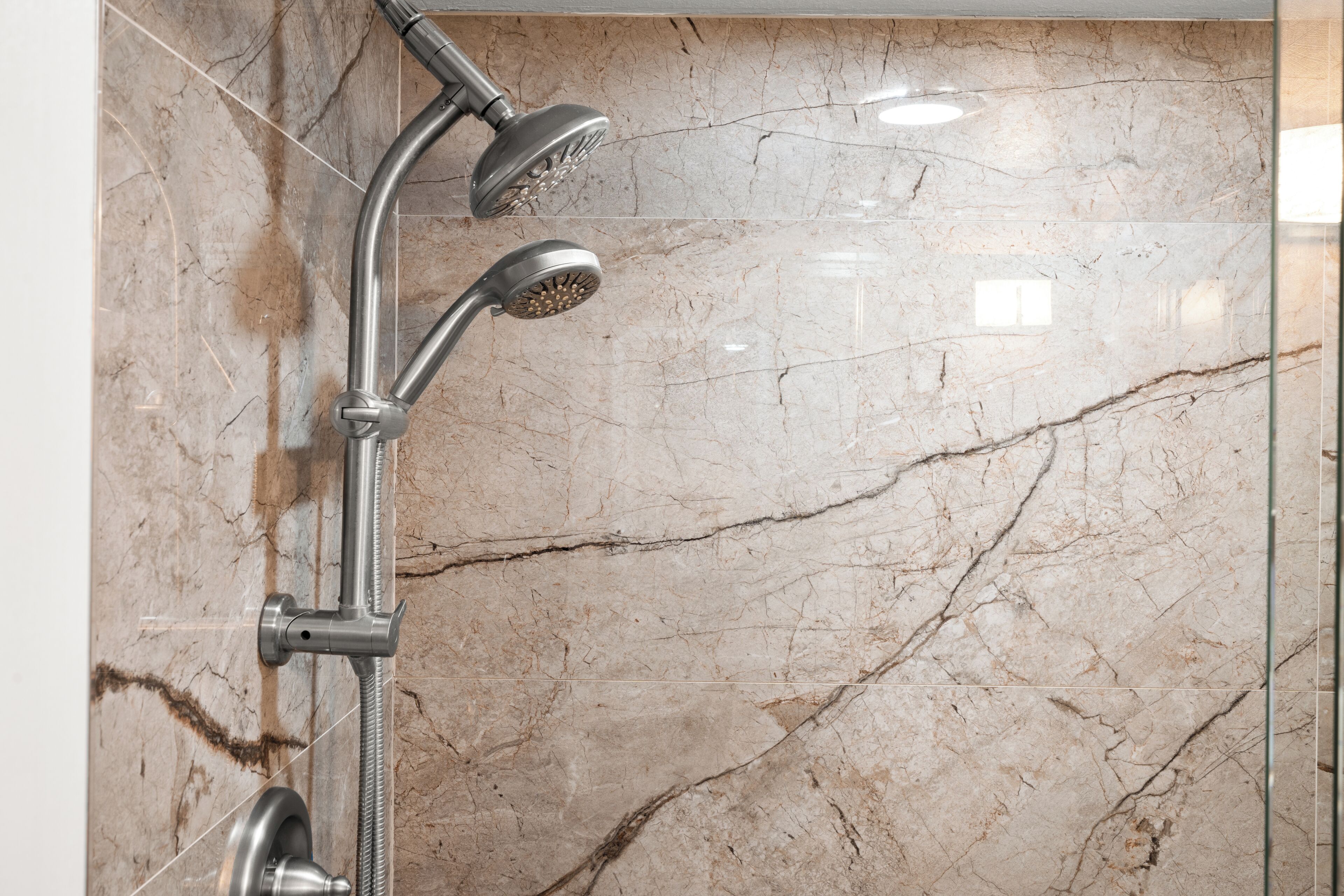A modern shower with a handheld showerhead and a fixed showerhead, mounted on a wall with a marble finish.