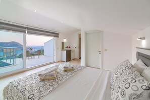 A modern hotel room with a balcony, a bed with patterned bedding, and a view of the sea. - Fantastic 3-bed Modern Villa with stunning views of Kalkan Bay from every level (Kalkan)