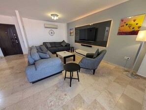 Ein modernes Wohnzimmer mit einer Couch, einem Sessel, einem Couchtisch und einem an der Wand befestigten Flachbildfernseher.