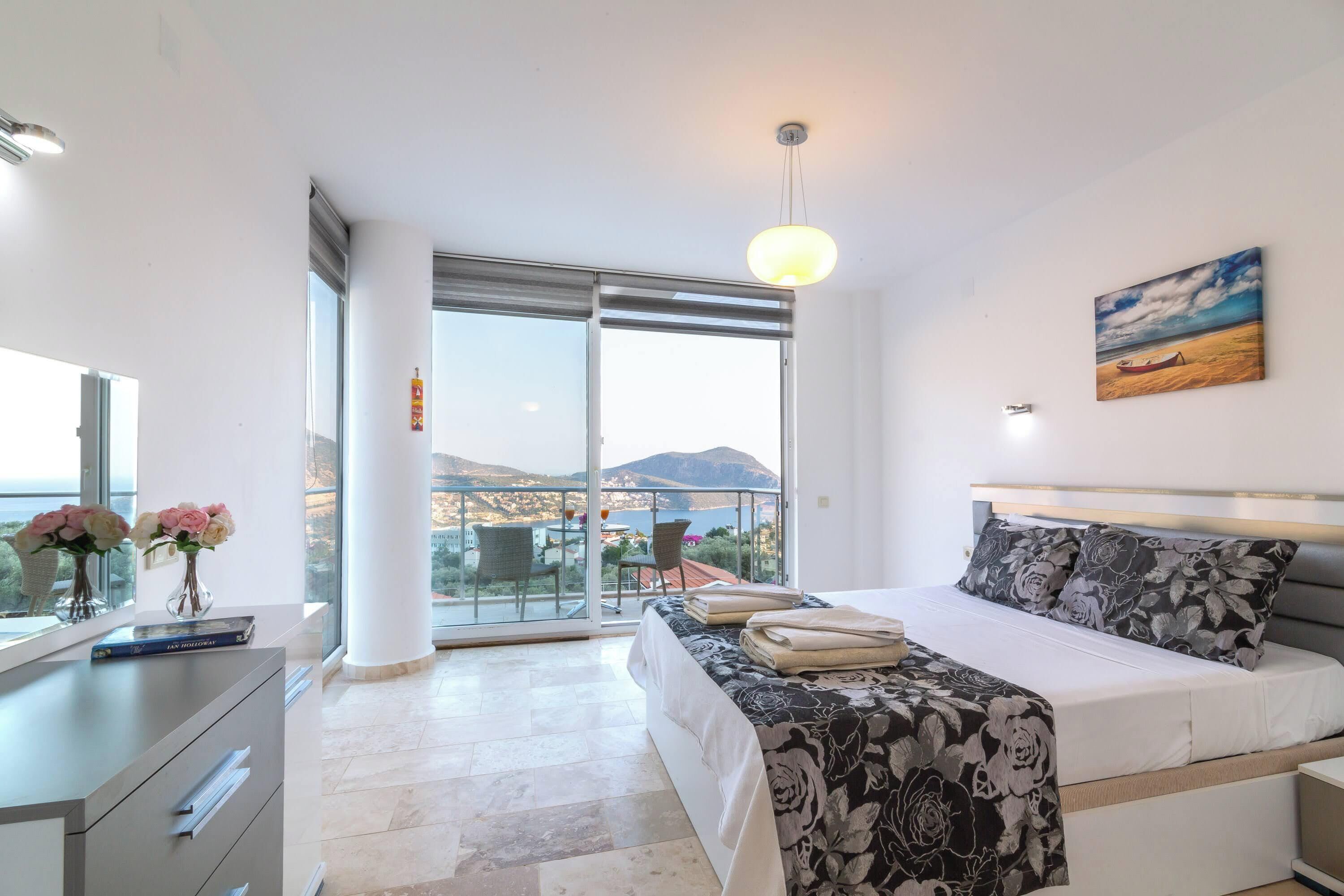 A modern bedroom with a bed, a desk, and a view of the sea.