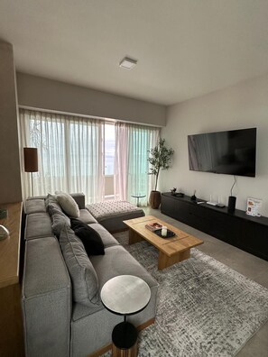 A modern living room with a grey sofa, a round coffee table, and a flat-screen TV mounted on the wall. - Private terrace with spectacular ocean views and beautiful sunrises (Tijuana)