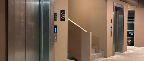 Un espace d’ascenseur doté de portes métalliques, d’une main courante et d’un escalier menant à un autre ascenseur.