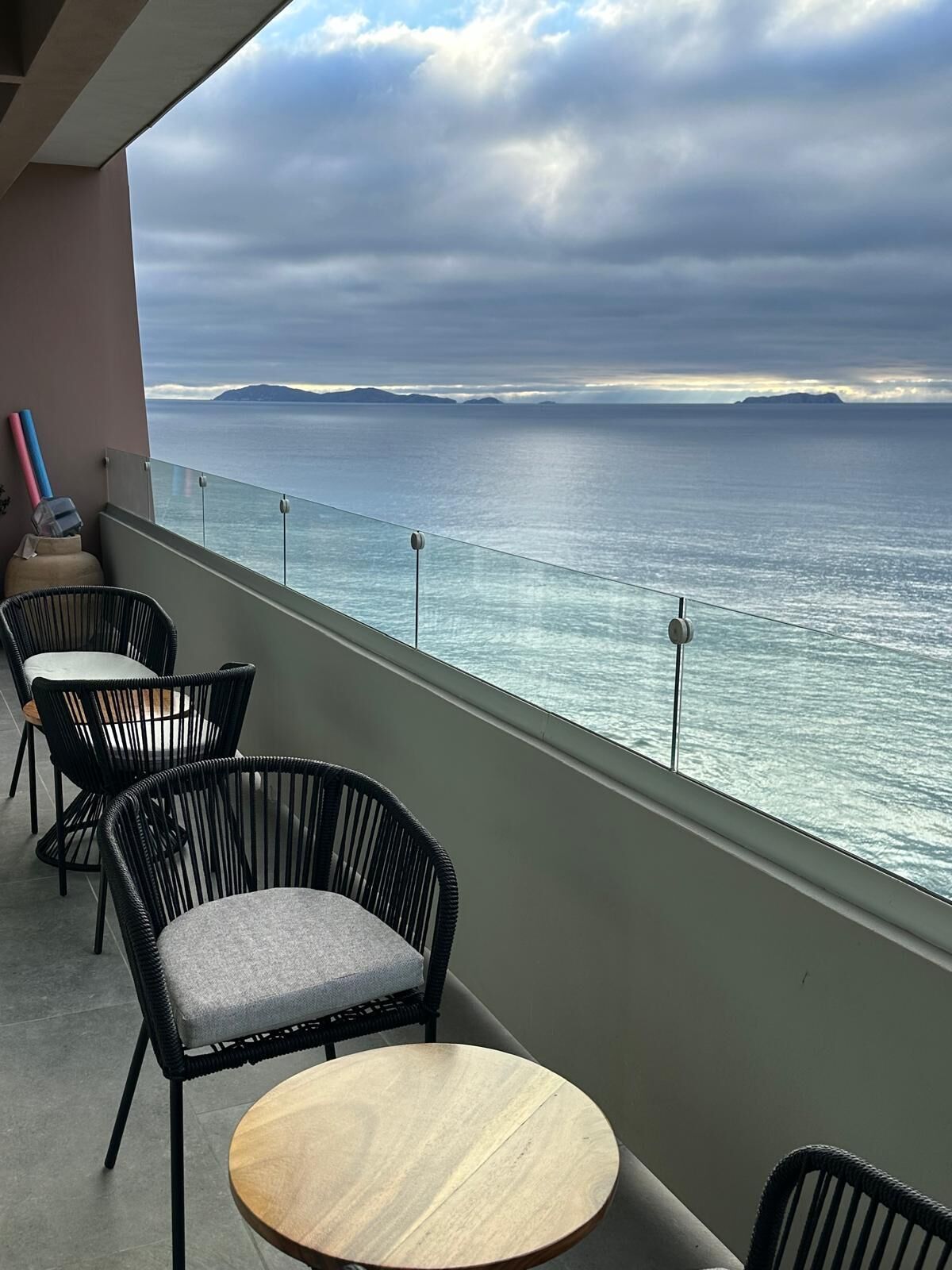 A balcony with a view of the sea, featuring wicker chairs and a round table.