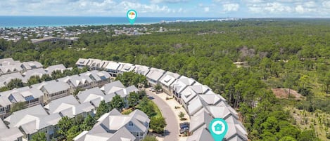 A residential area with a curved road, houses with similar architecture, and a dense forest in the background.