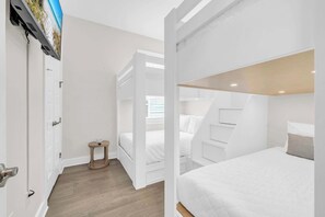 A bedroom with a bunk bed, a small bedside table, and a television mounted on the wall. - Gathered by the Sea by Stay on 30a (Inlet Beach)