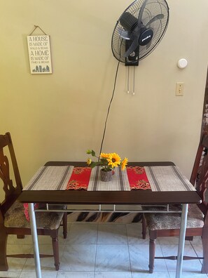 A dining table with a vase of sunflowers, a wall-mounted fan, and a sign with a home-related quote. - Rockery Villa Cozy Hideaway for Couple. (Port Antonio)