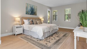 Une chambre à coucher avec un lit, des tables de chevet, un ventilateur de plafond, un tableau et une fenêtre avec des stores.