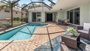 Une piscine avec un patio en briques, du mobilier d’extérieur et un espace couvert offrant une vue sur le quartier environnant.