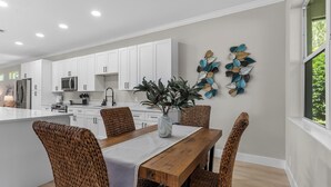Une cuisine moderne avec des meubles blancs, un îlot central et un coin repas doté de chaises en osier.