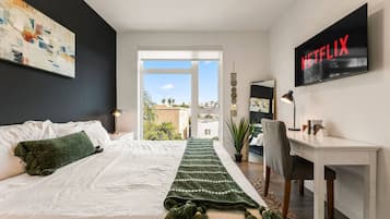 Une chambre moderne avec un grand lit, un bureau, une télévision et une vue sur la ville.