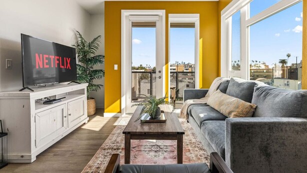Un salon équipé d’un téléviseur, d’un canapé, d’une table basse et offrant une vue sur la ville grâce à de grandes fenêtres.